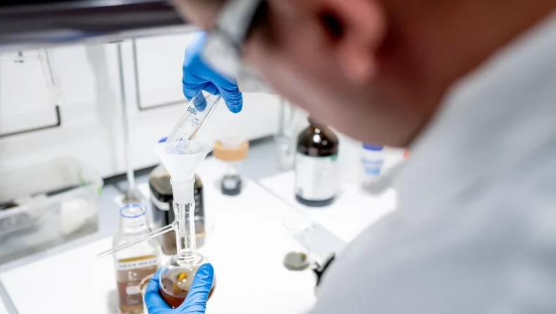 Dr rer. nat. Albert Paparo filling an oil sample into a glass container in the high-tech laboratory.