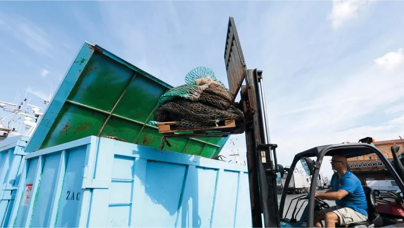 Roberto Guerini, President of the BioDesign Foundation, reaches into a pile of old fishing nets made of polypropylene, polythene and nylon to throw them into a shipping container for disposal.