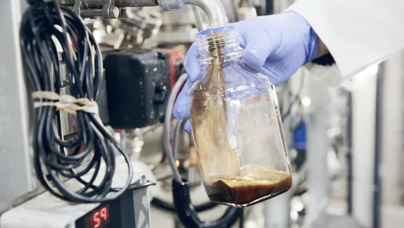 Hot pyrolysis oil flows out of a pipe into a glass container.